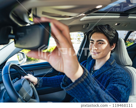Photo of a smiling male driver adjusting the rearview mirror in his car 119468111