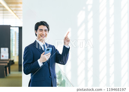 一位男性商人拿著智慧型手機在辦公大樓大廳提出建議 119468197