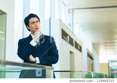 A male business person thinking deeply in the lobby of an office building 119468233