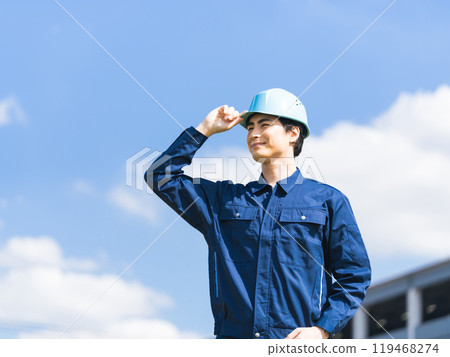 A worker stands in front of a factory-like building under a blue sky A worker stands in front of a factory-like building under a blue sky 119468274