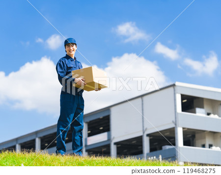 A delivery staff member carrying luggage in front of a building that looks like a logistics center 119468275