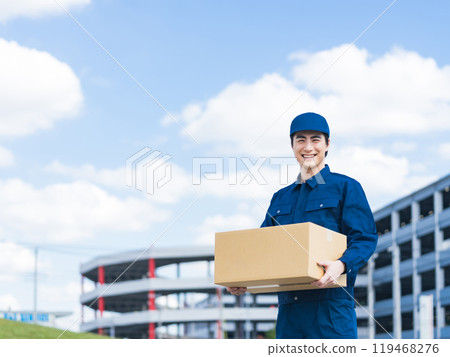 A delivery staff member carrying luggage in front of a building that looks like a logistics center 119468276
