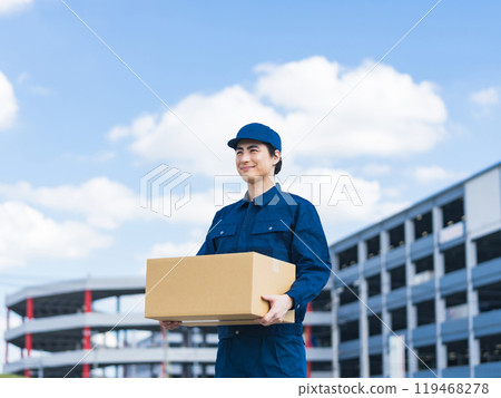 A delivery staff member carrying luggage in front of a building that looks like a logistics center 119468278
