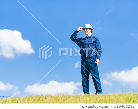 一名工人站在藍天下的草地上抬頭仰望 119468282