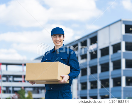 A delivery staff member carrying luggage in front of a building that looks like a logistics center 119468284