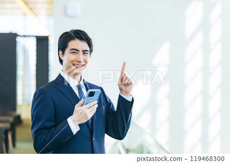 Male business person holding a smartphone and recommending something in the lobby of an office building 119468300