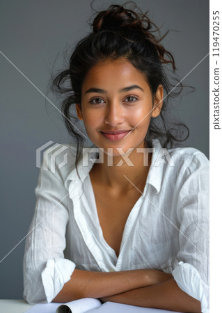 Confident young Indian woman in white shirt with natural make-up sitting at table. Portrait, vertical shot 119470255