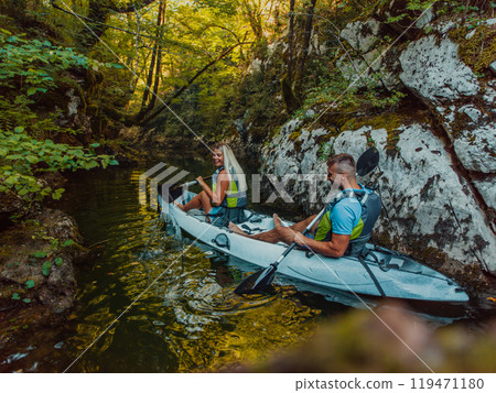 A young couple enjoying an idyllic kayak ride in the middle of a beautiful river surrounded by forest greenery 119471180