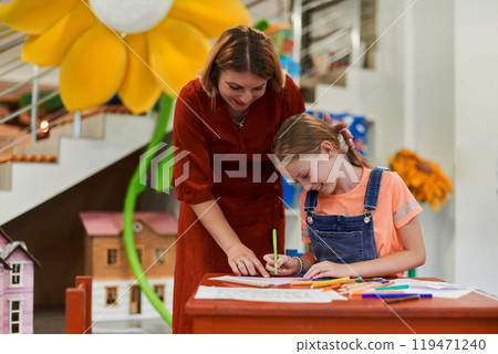 Creative kids during an art class in a daycare center or elementary school classroom drawing with female teacher. 119471240