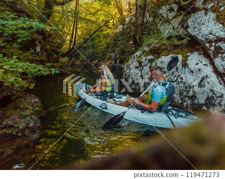 A young couple enjoying an idyllic kayak ride in the middle of a beautiful river surrounded by forest greenery A young couple enjoying an idyllic kayak ride in the middle of a beautiful river surrounded by forest greenery 119471273