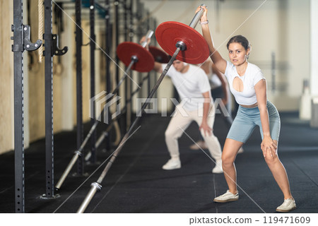 Young woman training with barbell with one arm 119471609