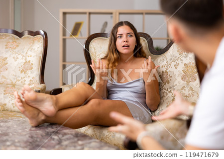 Outraged woman scolding husband while sitting on sofa in room Outraged woman scolding husband while sitting on sofa in room 119471679