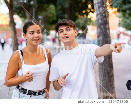 Happy young couple pointing while looking at something on city street Happy young couple pointing while looking at something on city street 119471806