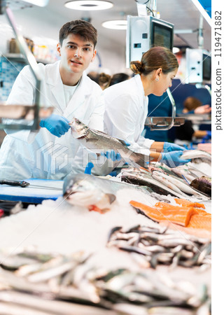 Smiling salesman demonstrating seabass in fish store 119471882