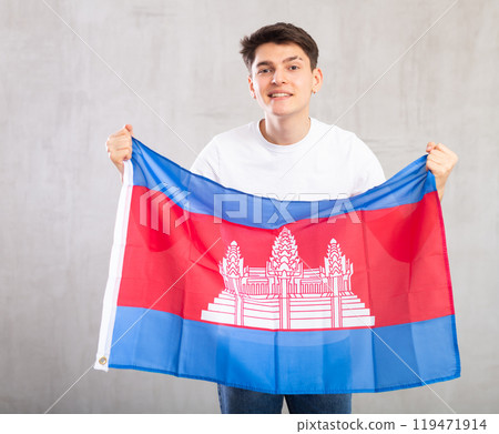 Happy young man holding flag of Cambodia against unicoloured background 119471914