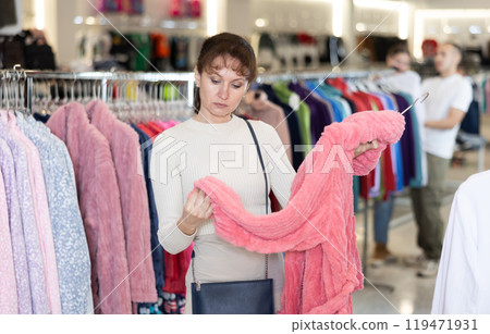 Middle-aged woman choosing convenient bathrobe in clothing store Middle-aged woman choosing convenient bathrobe in clothing store 119471931