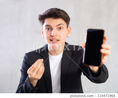 Agent in black suit jacket shows dark empty mobile phone screen and points at device with his hand 119471968