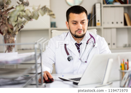 Portrait of male doctor using laptop in office Portrait of male doctor using laptop in office 119471970