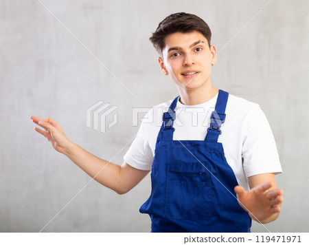 Young experienced worker in blue jumpsuit is actively gesticulating, looking up to right 119471971