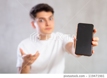 Enthusiastic young man showing screen of mobile phone excitedly 119471981