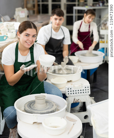 Young woman holding clay bawl at pottery wheel Young woman holding clay bawl at pottery wheel 119471990