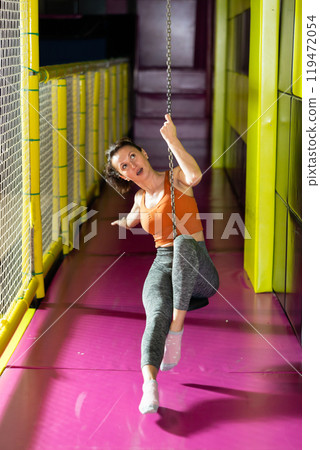 Excited woman swinging on indoor zip line at modern play center Excited woman swinging on indoor zip line at modern play center 119472054
