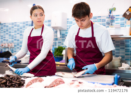 Proficient sellers processing seabass on table board in fish store 119472176
