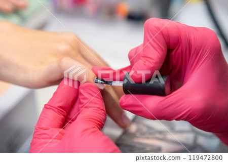 Professional manicure in a salon applying gel polish with a base coat on nails by manicurist in rubber gloves Professional manicure in a salon applying gel polish with a base coat on nails by manicurist in rubber gloves 119472800