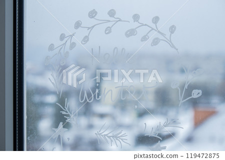 Sustainable responsible holiday decor. Hello winter text painted on window glass indoor at home. Christmas winter decoration. White pattern. Snow art tracery on season. Diy Sustainable responsible holiday decor. Hello winter text painted on window glass indoor at home. Christmas winter decoration. White pattern. Snow art tracery on season. Diy 119472875