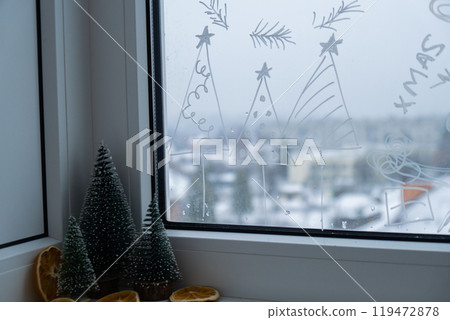 Painted window with white marker. Christmas tree decoration on big clear window. Snowy winter outside. Zero waste decor conscientious celebration 119472878