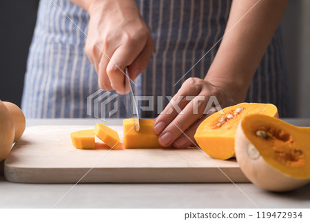 Woman hand holding kitchen knife and cutting butternut squash on wooden board, Homemade cooking 119472934