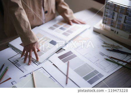 Female architect choosing color swatch sample to design interior of building project on blueprint 119473228