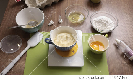 Process of weighing almond flour on electronic scale in kitchen at home. Inventory for preparation of dough. Scales, utensils on wooden table. Process of weighing almond flour on electronic scale in kitchen at home. Inventory for preparation of dough. Scales, utensils on wooden table. 119473653