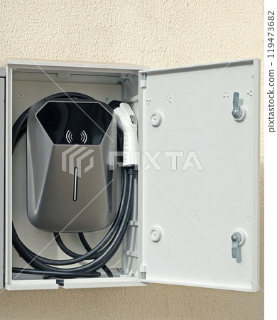 Electric Vehicle Charging Station in house on yard. Mini device on wall. Electric Vehicle Charging Station in house on yard. Mini device on wall. 119473682