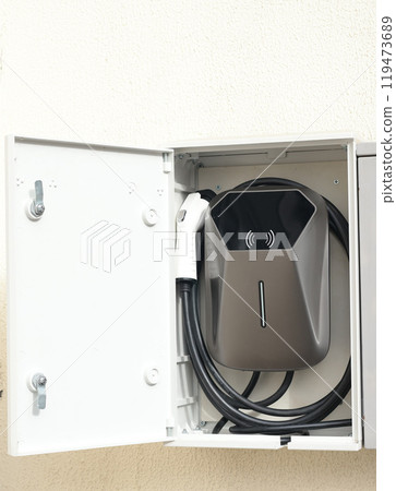 Electric Vehicle Charging Station in house on yard. Mini device on wall. Electric Vehicle Charging Station in house on yard. Mini device on wall. 119473689
