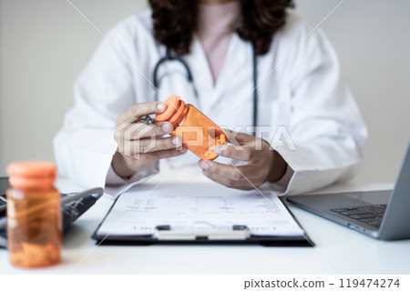 Female doctor holding a medicine bottle is checking the quality of medicine for any side effects the patient or not and recording patient information at the hospital. medical and health care concept 119474274