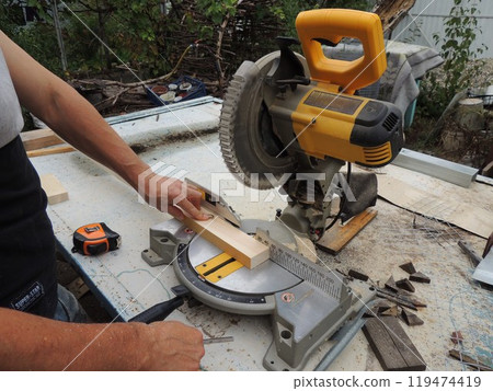 carpenter working at a miter saw, cutting the edge of a plank, processing the ends of wooden skirting boards on a miter saw, sawing off part of the skirting board at the corners of a saw 119474419