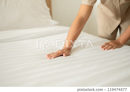 The hotel maid cleans and makes the bed in the hotel room The hotel maid cleans and makes the bed in the hotel room 119474877