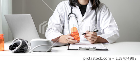 Female doctor holding a medicine bottle is checking the quality of medicine for any side effects the patient or not and recording patient information at the hospital. medical and health care concept 119474992