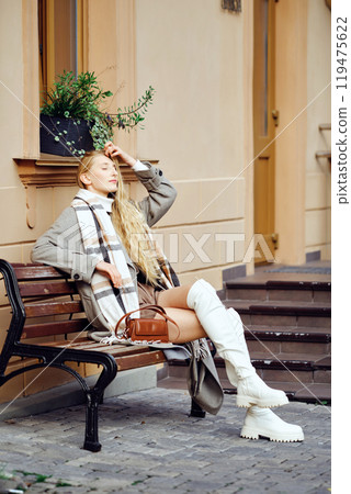 A woman relaxing on a bench in a stylish outfit during a sunny day in the city A woman relaxing on a bench in a stylish outfit during a sunny day in the city 119475622