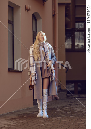 A young woman in a stylish autumn outfit left the house and exposed her face to the rays of the sun 119475624