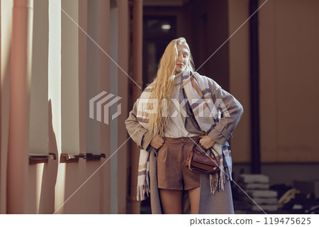 Stylish woman with long hair stands near the house under bright rays of sun 119475625