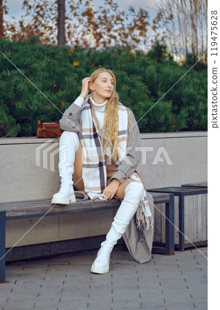 Young woman in stylish boots sitting on a bench during autumn in a sleek urban environment Young woman in stylish boots sitting on a bench during autumn in a sleek urban environment 119475628