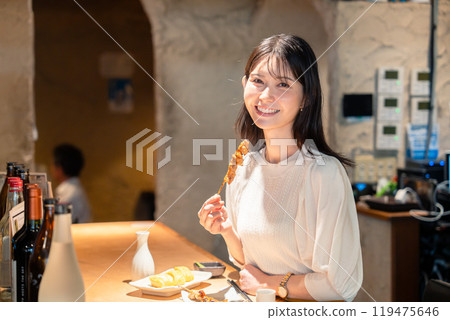 A woman sitting alone at a counter eating yakitori 119475646