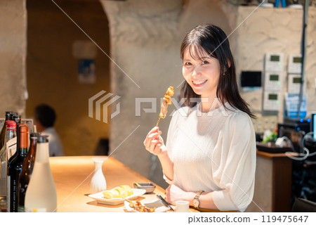 A woman sitting alone at a counter eating yakitori 119475647