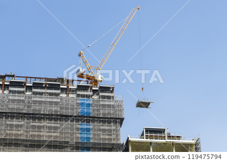 Low-angle view of cranes and steel structures of building construction with a blue sky background. Low-angle view of cranes and steel structures of building construction with a blue sky background. 119475794