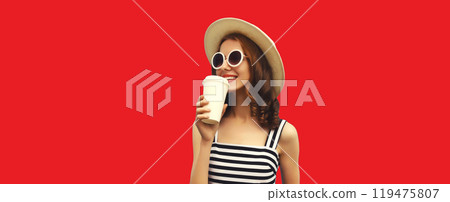 Happy smiling young woman drinking juice or coffee wearing summer hat, glasses on red background Happy smiling young woman drinking juice or coffee wearing summer hat, glasses on red background 119475807