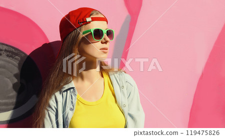 Stylish young girl in baseball cap, glasses, modern teenager girl posing against the graffiti wall 119475826