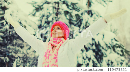 Happy cheerful smiling young woman in colorful knitted hat, enjoys weather in winter snowy park 119475831