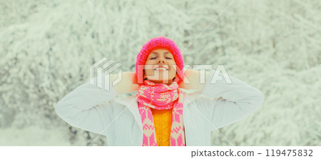 Happy cheerful smiling young woman in colorful knitted hat, enjoys weather in winter snowy park Happy cheerful smiling young woman in colorful knitted hat, enjoys weather in winter snowy park 119475832